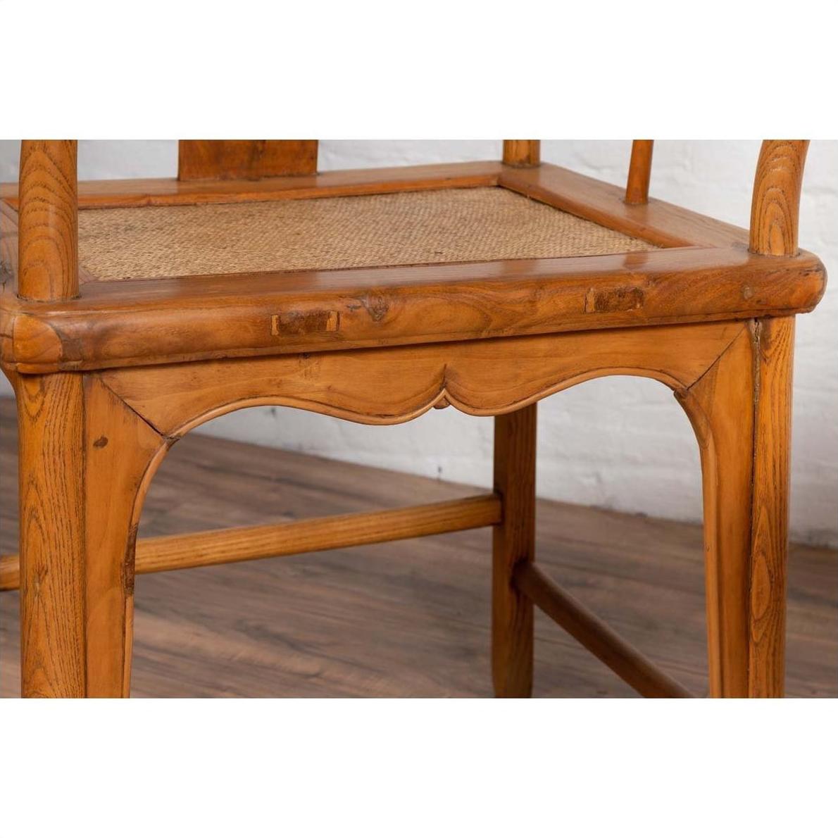 Close-up of brown wood and rattan Ming Dynasty style armchair with curving arms, indoor setting.