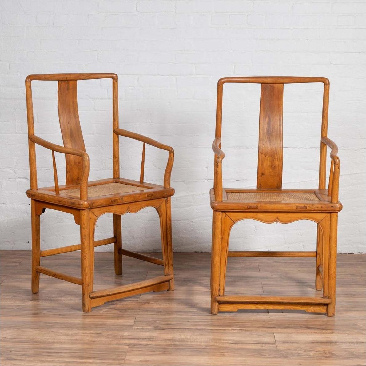 Brown wood and rattan Ming dynasty style wedding armchairs with curved arms, on a wooden floor by a white wall indoors.