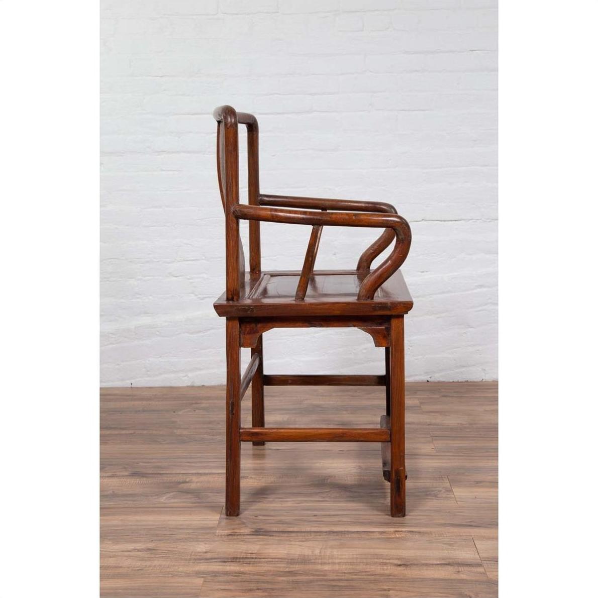 Brown wooden wedding chair with carved medallion and curving arms, side view, indoors against white brick wall.