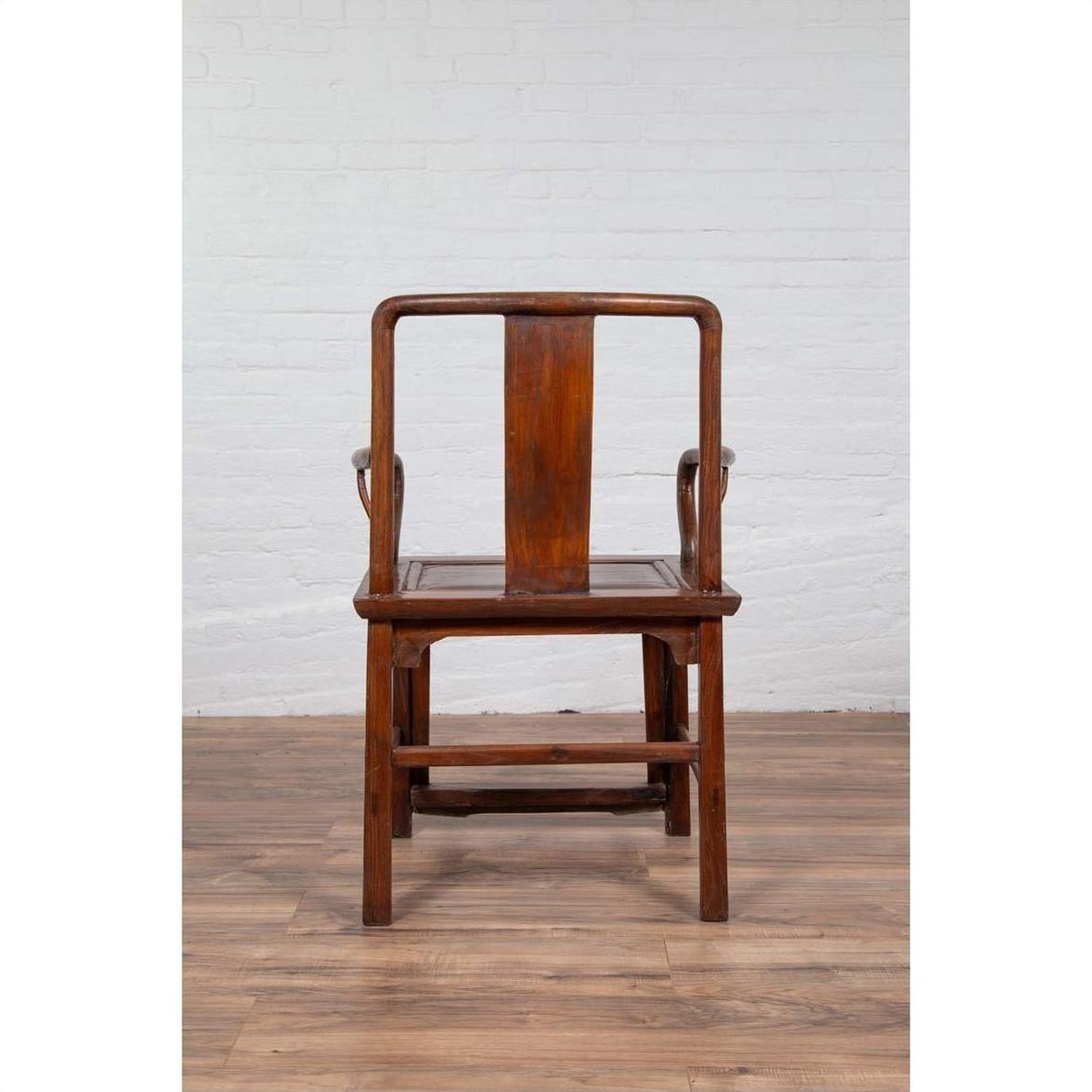 Brown wooden wedding chair with carved medallion and curving arms, placed next to a white brick wall indoors.