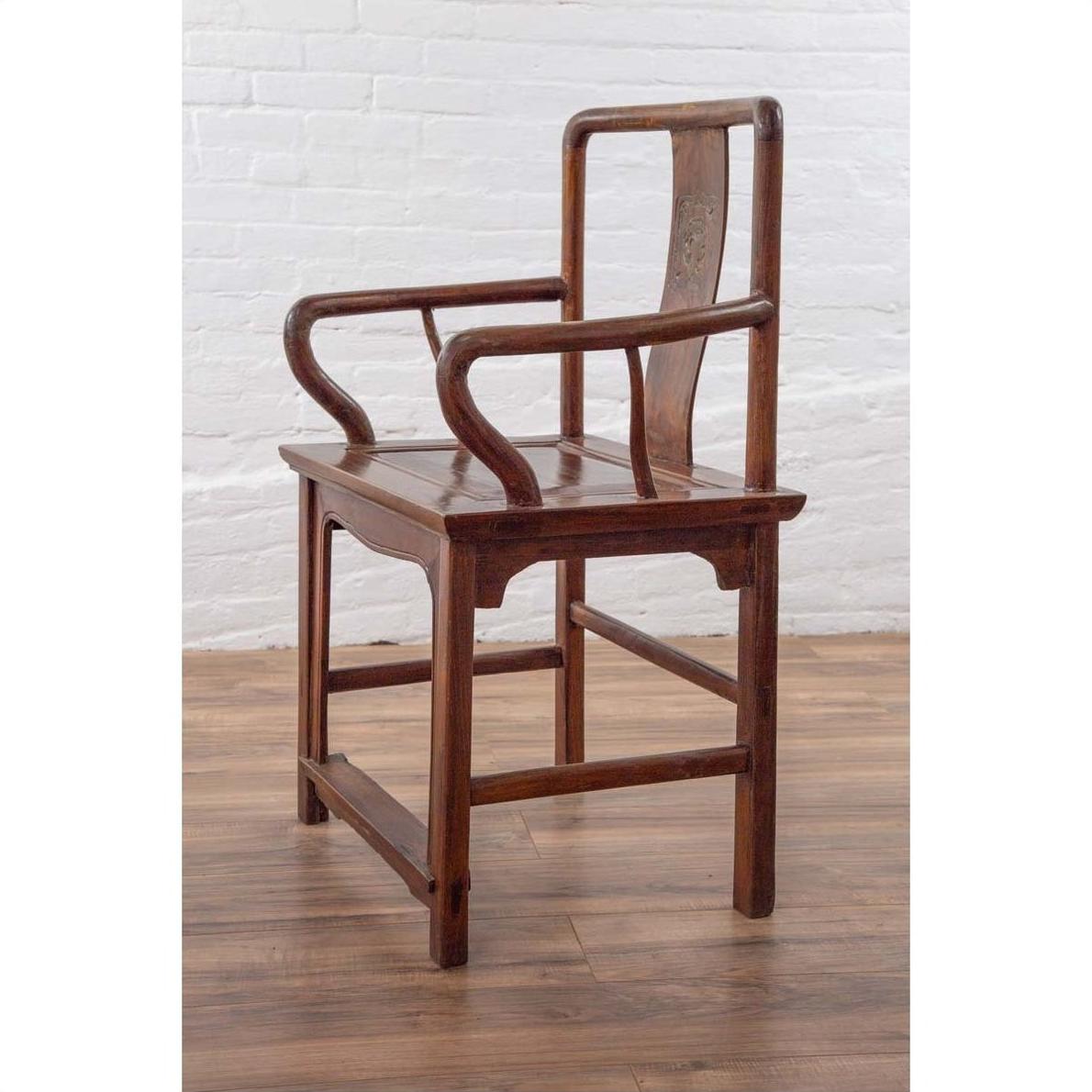 Brown wooden wedding chair with carved medallion and curving arms placed indoors by a white brick wall.