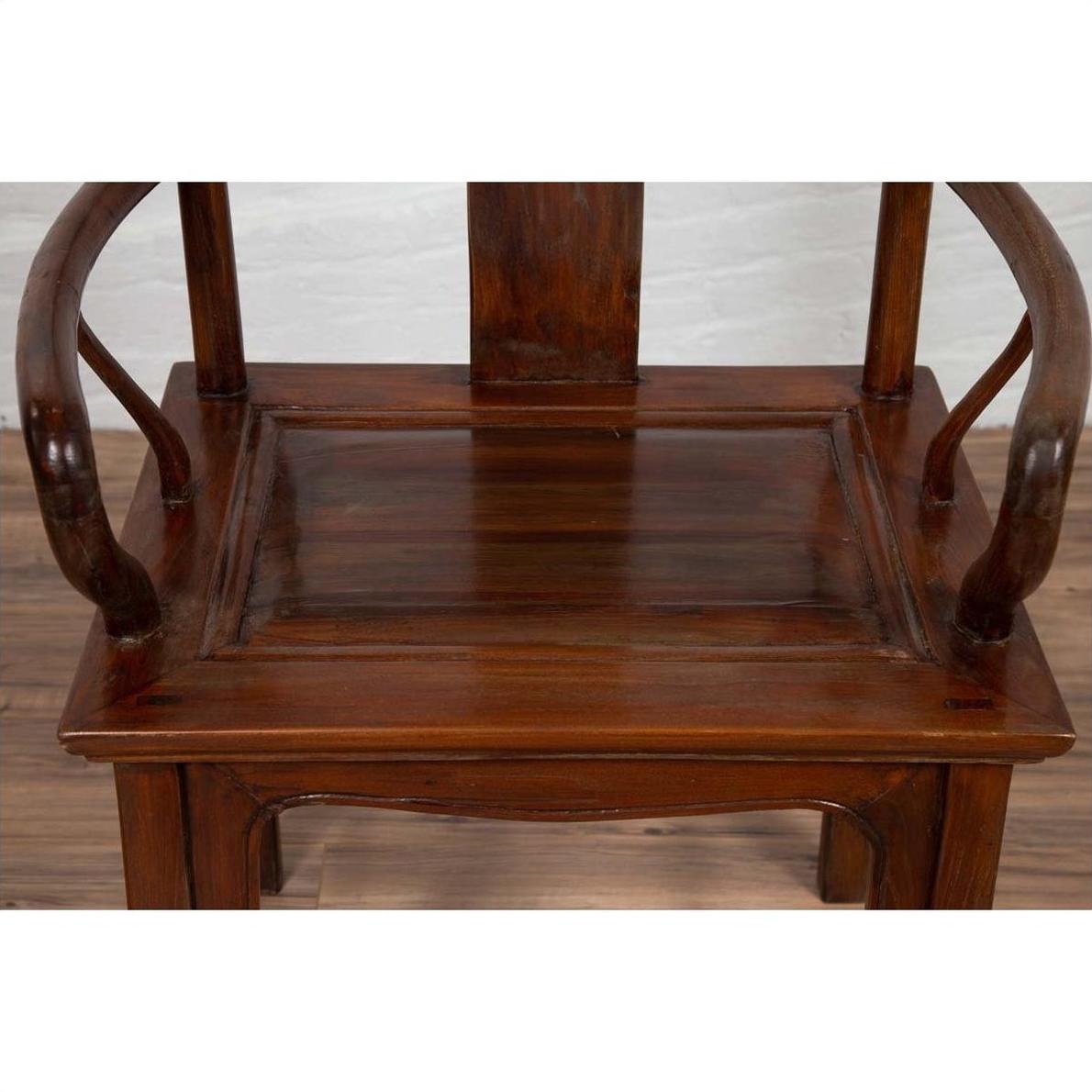Close-up of brown wooden Ming Dynasty style wedding chair with carved medallion and curved arms on wood floor.