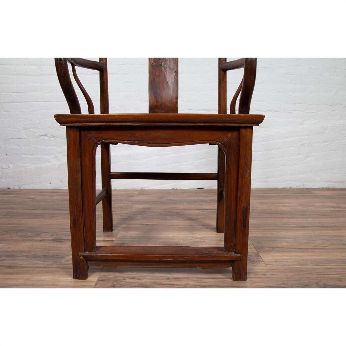 Brown wooden Ming Dynasty style wedding chair with carved medallion and curved arms on a wooden floor indoors.