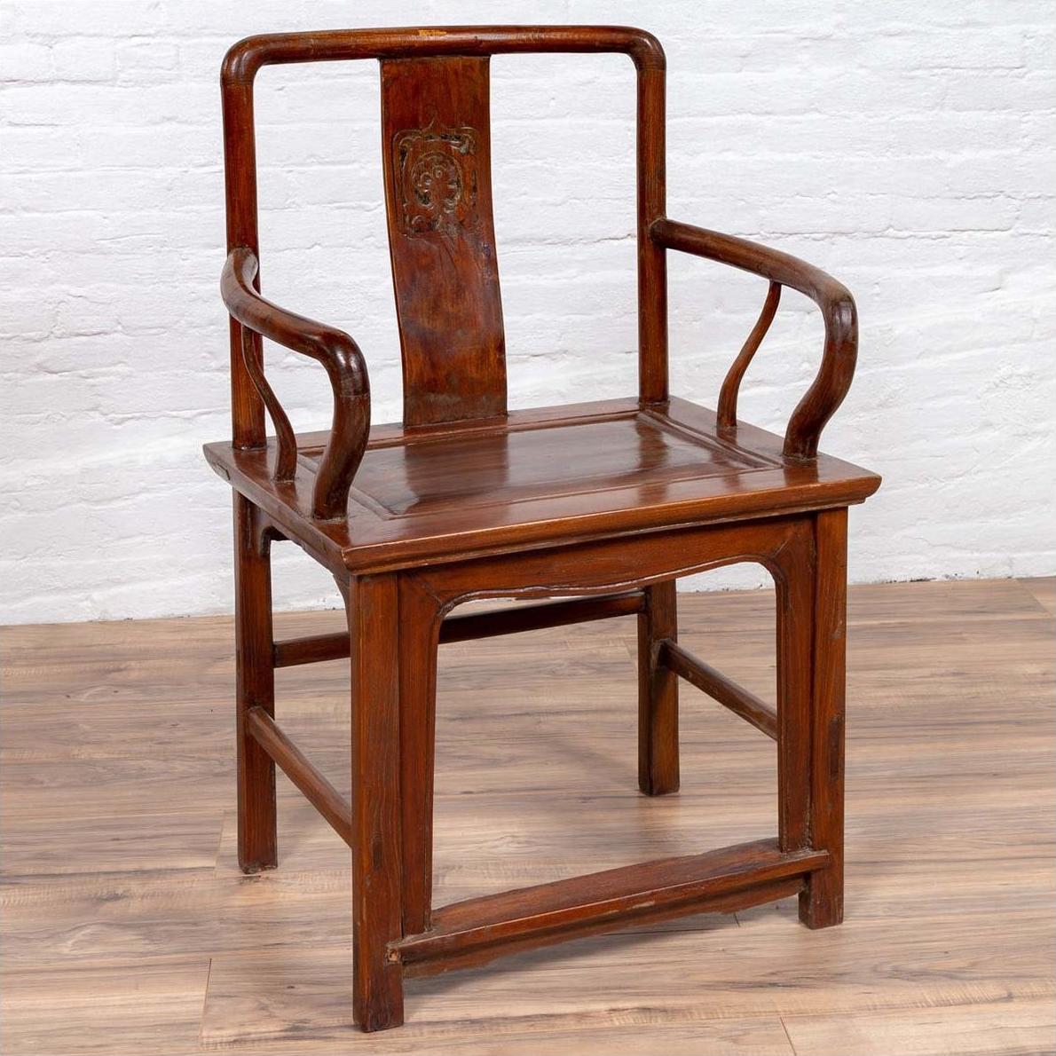 Brown wooden wedding chair with carved medallion and curving arms, placed on wood floor by a white brick wall indoors.