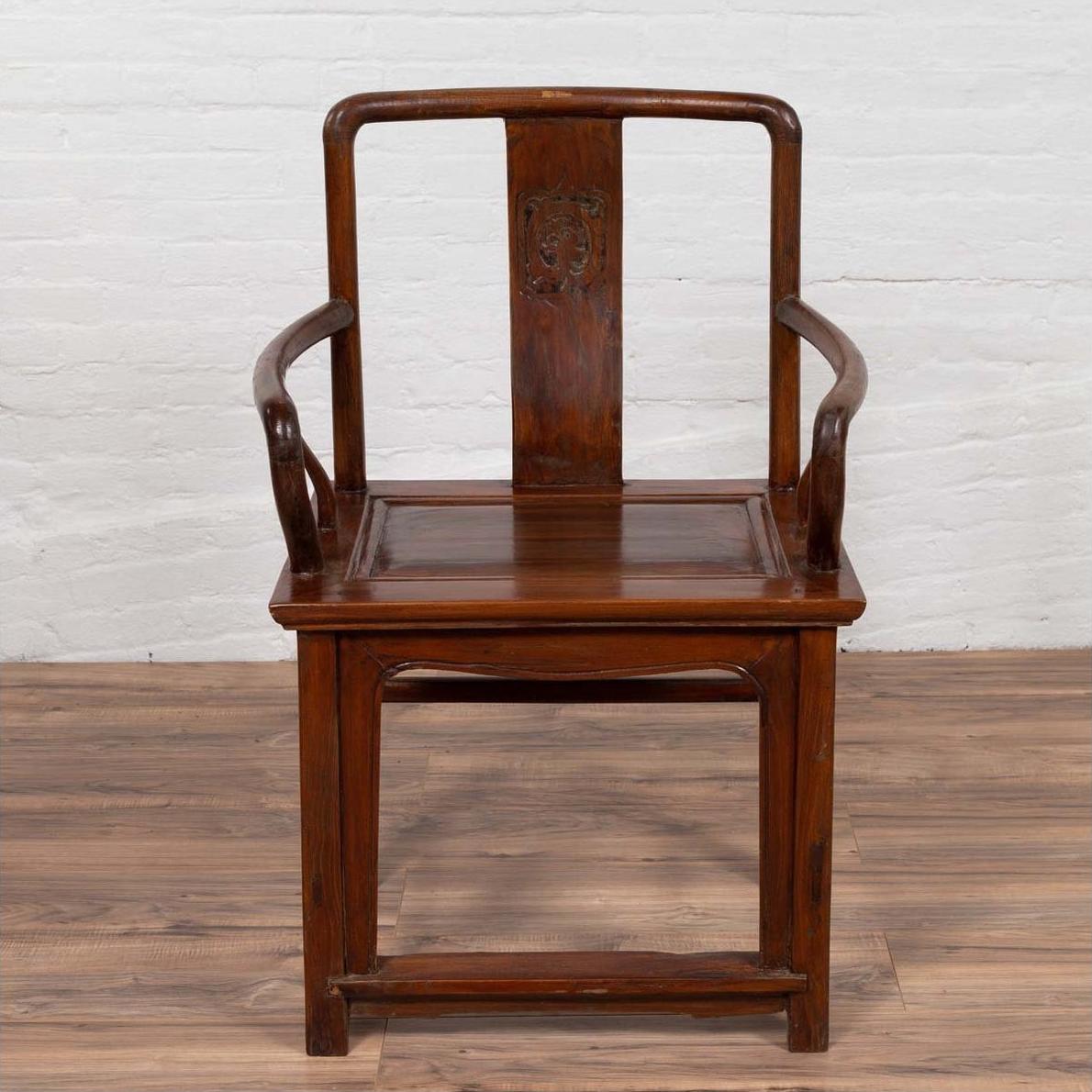 Brown wooden Ming Dynasty style wedding chair with carved medallion and curving arms on a wooden floor indoors.