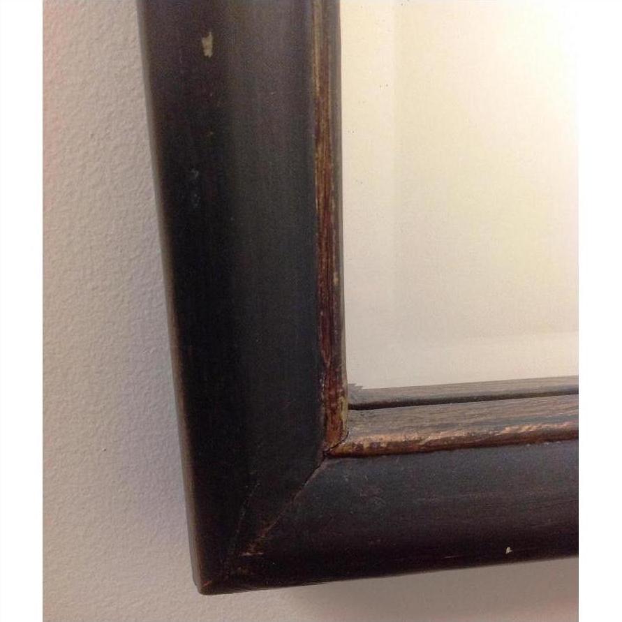 Close-up of dark brown wood mirror frame corner against a light-colored wall.