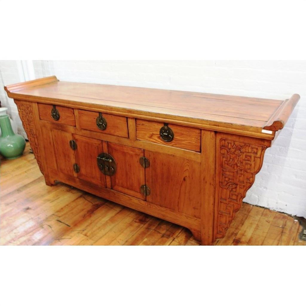 Natural wood altar coffer with ornate carvings and brass hardware, displayed on a wooden floor.