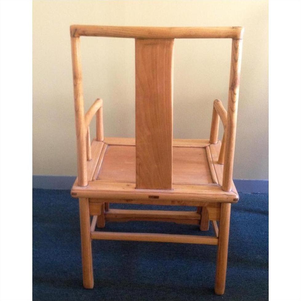 Natural wood chair with wide vertical backrest and armrests on a blue carpeted floor.