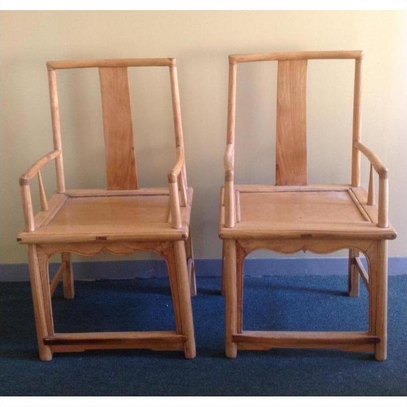 Natural wood chairs with tall, straight backs and armrests on blue carpet against a light wall, side by side.