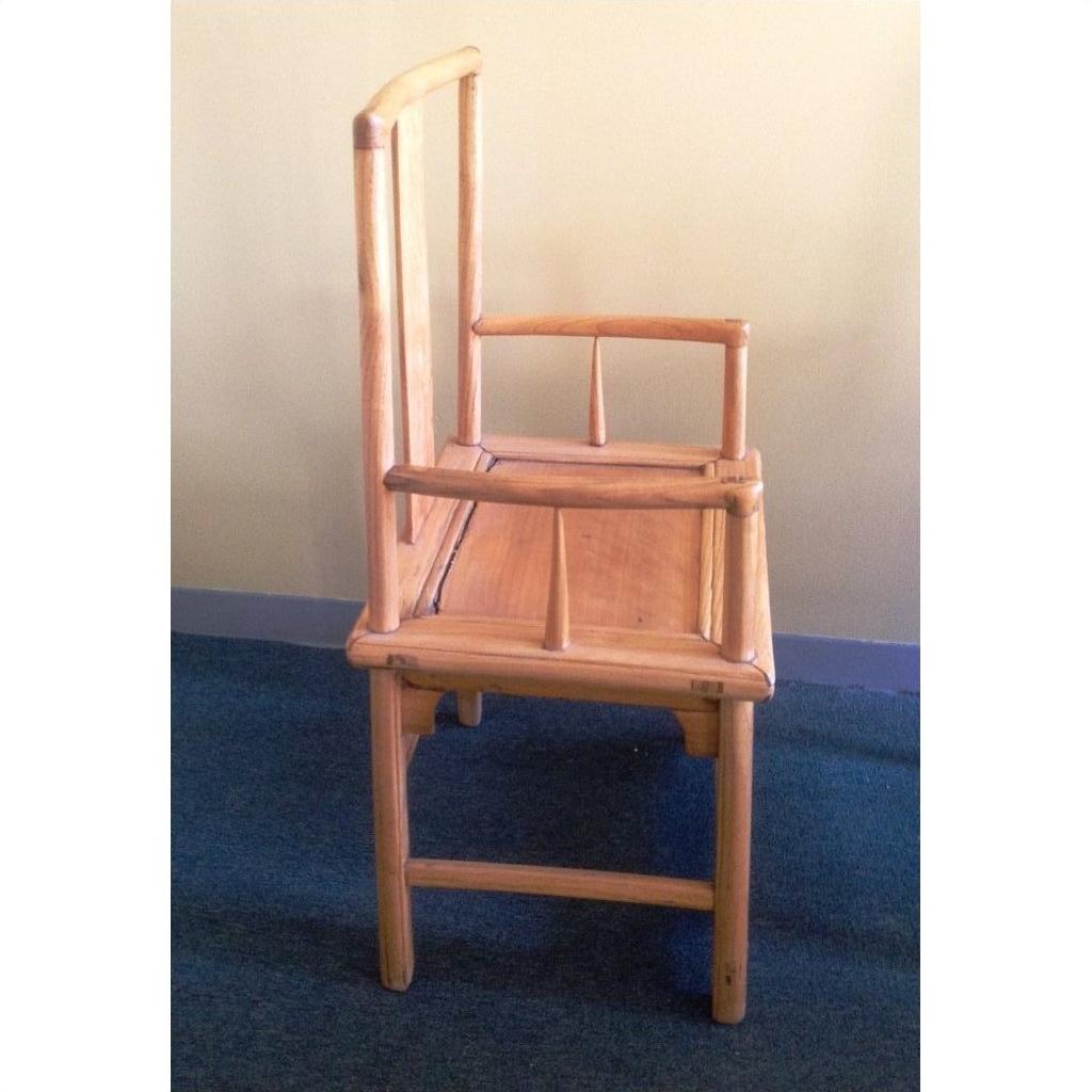 Natural wood chairs with uneven high armrests and a carved apron, showing an asymmetrical geometric silhouette.