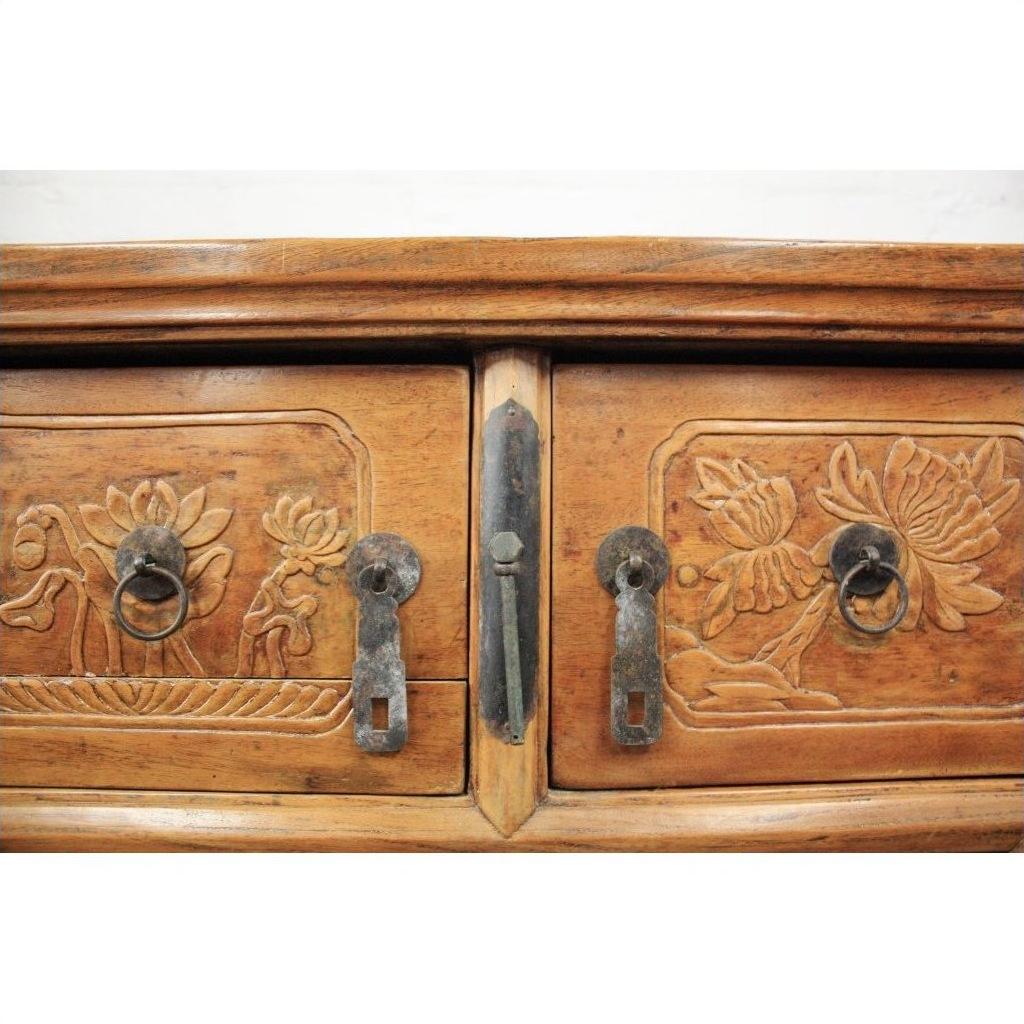 Close-up of natural elmwood cabinet doors with carved floral designs, metal handles, and keyholes.