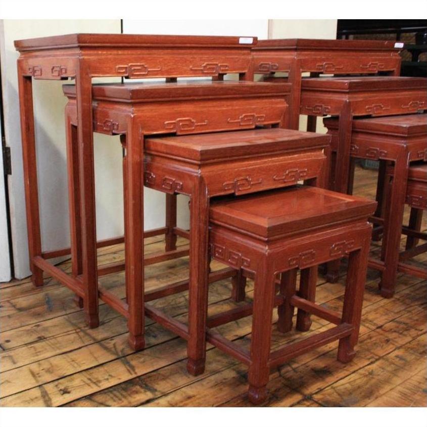 Four rosewood nesting tables with ornate carvings on a wooden floor against a cream-colored wall.