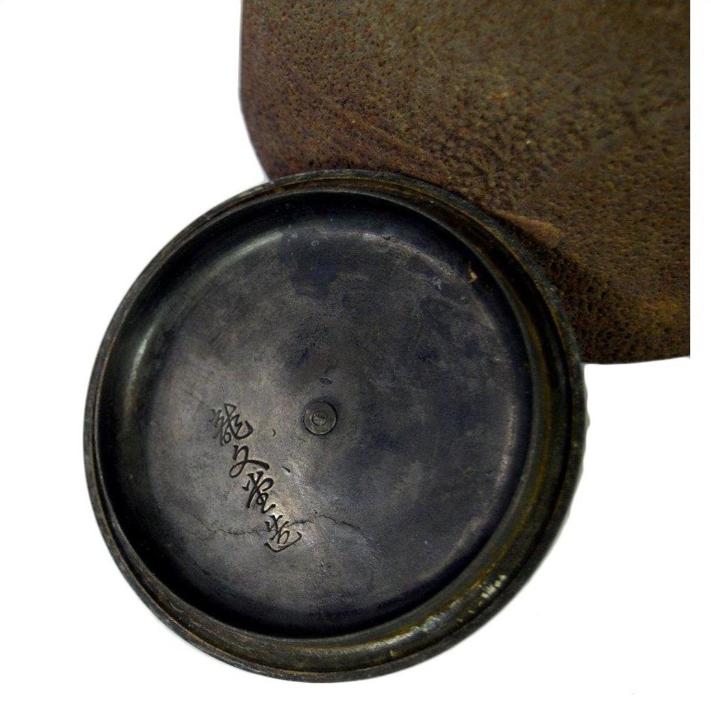Close-up of a dark metal Old Japanese teapot lid with Japanese characters inscribed underneath, in good condition.