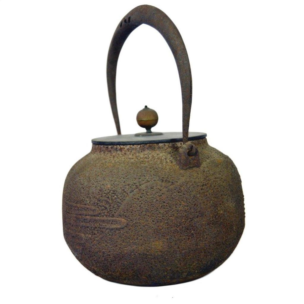 Black iron Japanese teapot with textured surface, curved handle, and small knob lid, close-up on neutral background.