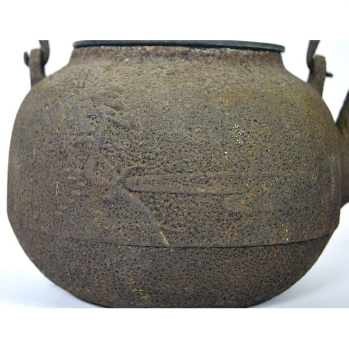 Close-up of a brown metal Japanese teapot with textured, rusty surface and faint markings, in used condition.