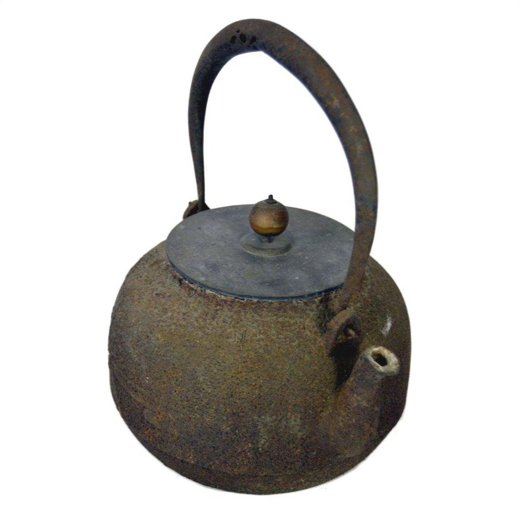 Used metal Japanese teapot with curved handle and lid, close-up on plain white background.