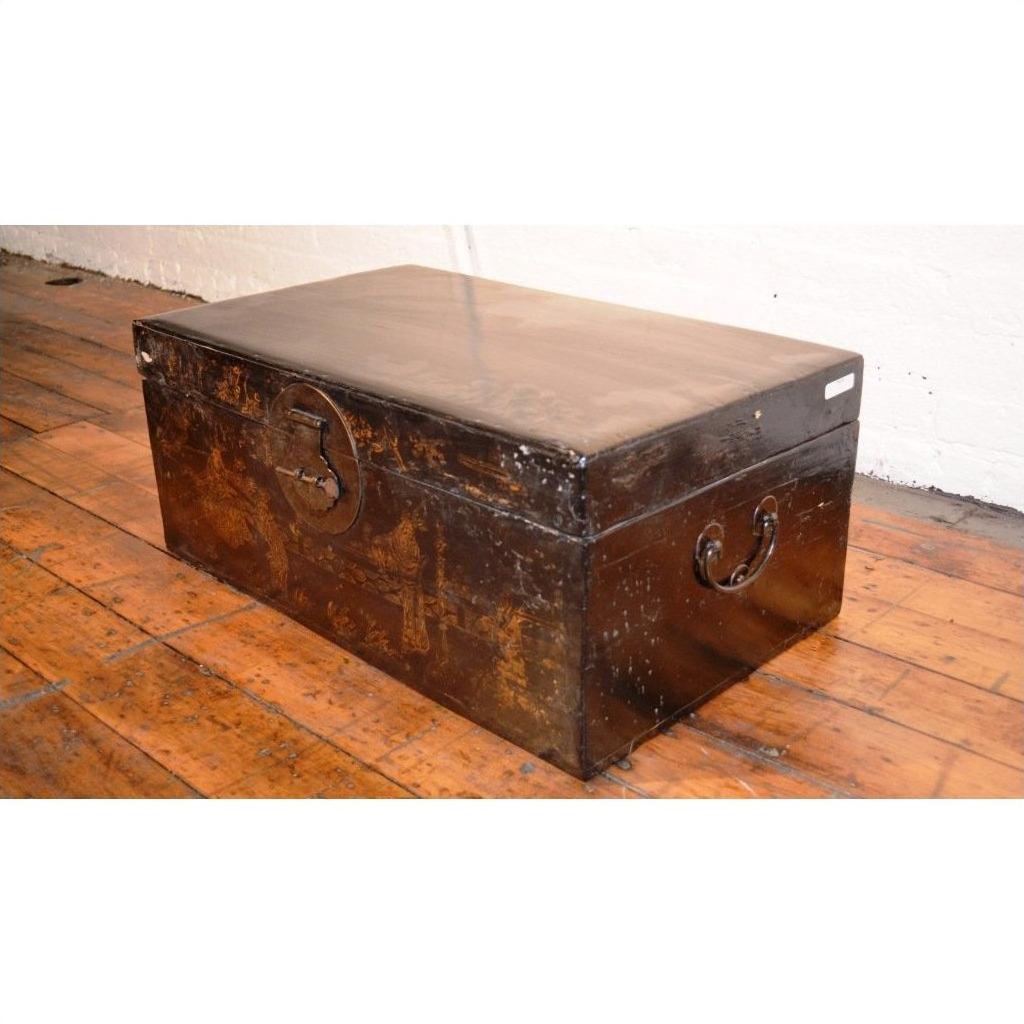 Large black lacquered trunk on wooden floor against a white wall, decorative storage furniture in home setting.