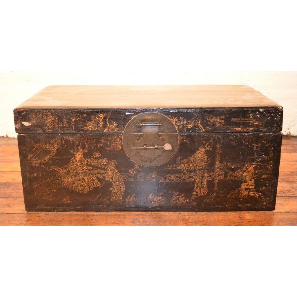 Black lacquer trunk with gold motifs and round metal clasp on a wooden floor.