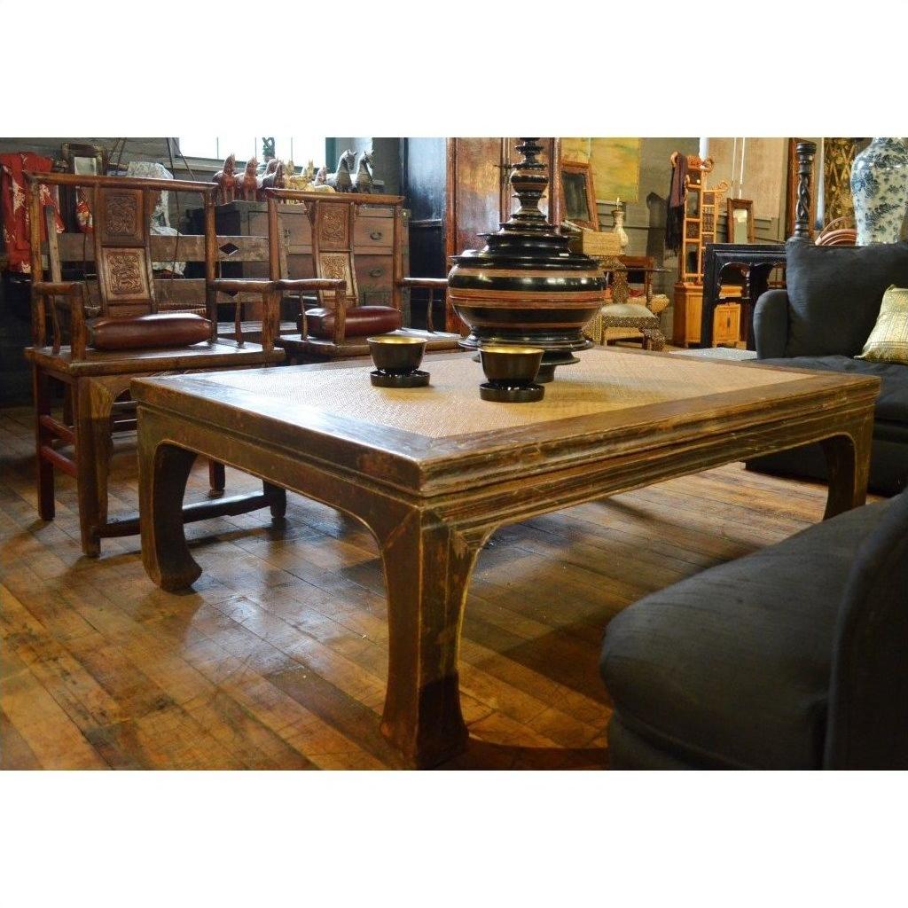 Black lacquer coffee table with bowls and vase, surrounded by sofas and wooden chairs in a vintage-style room.