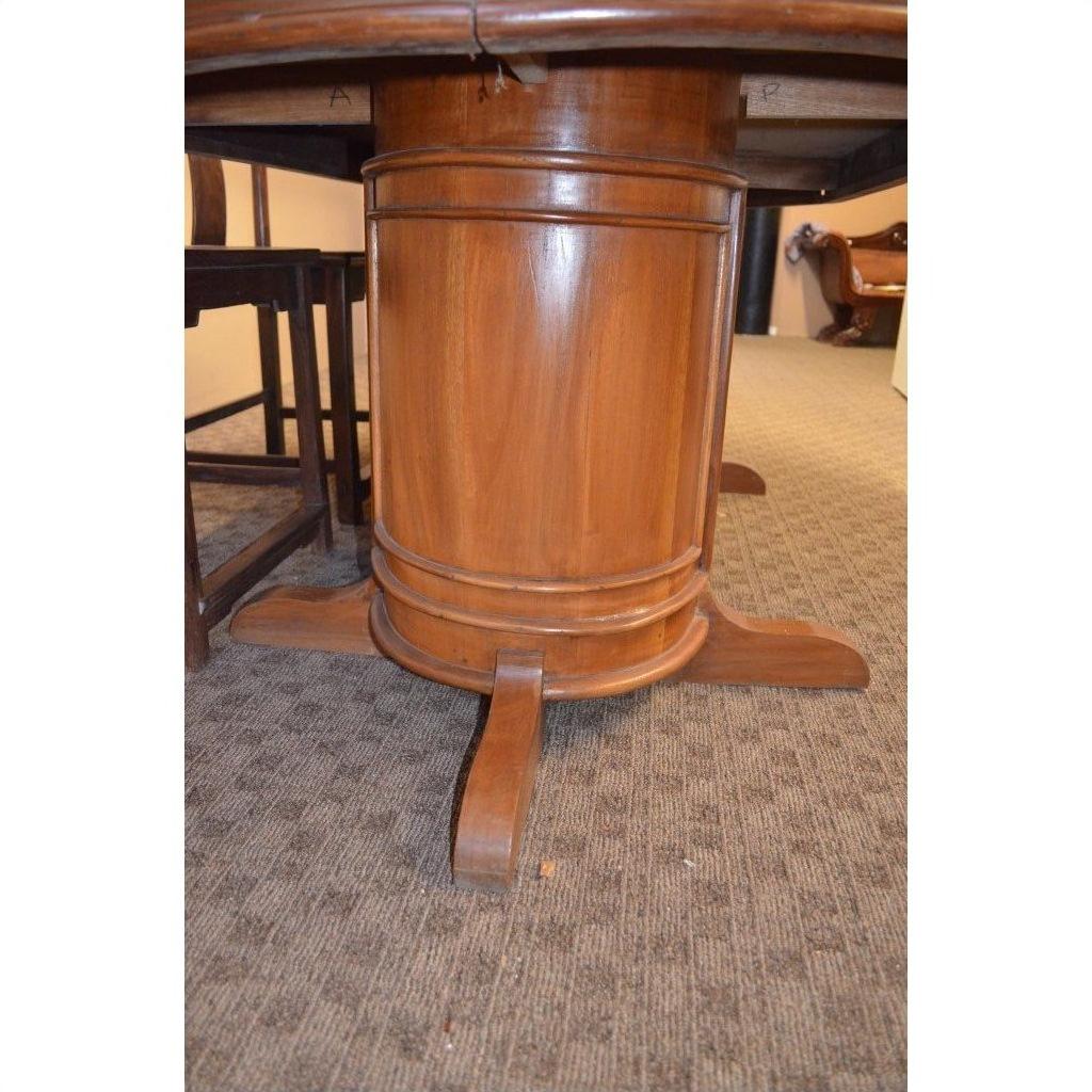 Close-up of dark wood pedestal dining table base with four feet on a light carpeted floor.