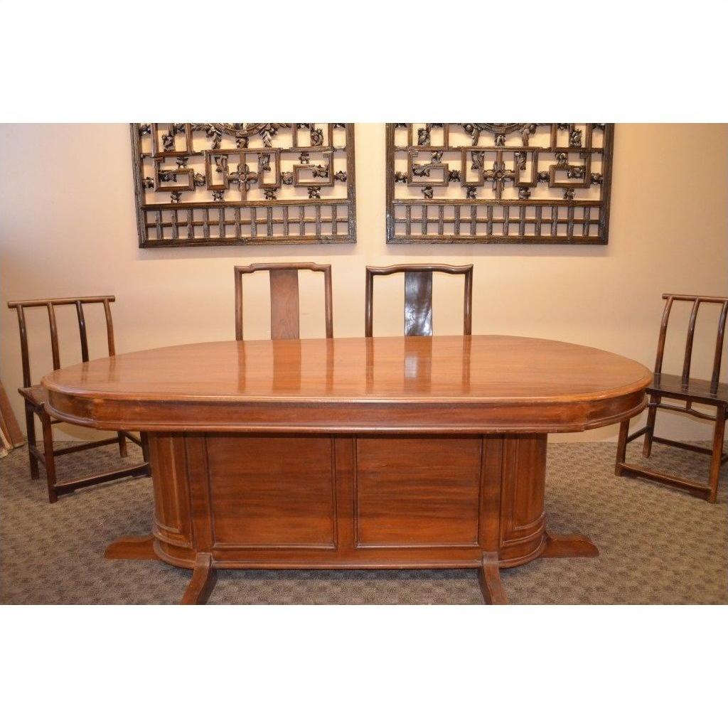 Brown wood oval pedestal dining table with matching chairs, set in a room with modern wall art.