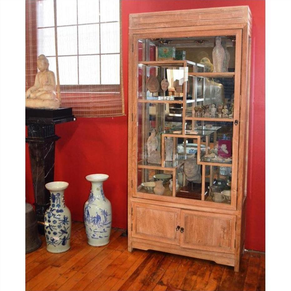 Brown teak display cabinet with glass doors, displaying figurines and blue and white vases, Thai statue beside.