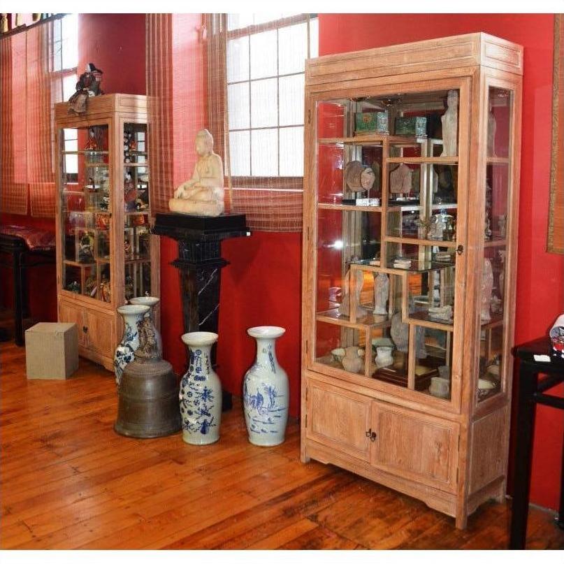 Vintage teak display cabinet from Thailand with ceramics inside, large vases and a statue in front on wood floors.