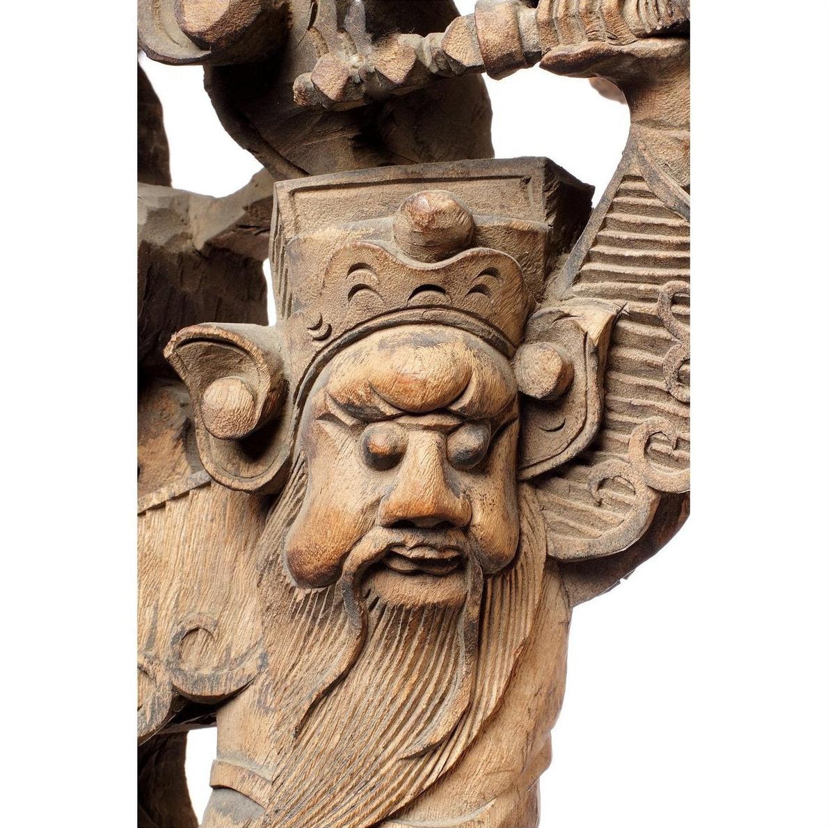 Close-up of a carved wood Chinese temple corbel character, 18th-century, crowned, bearded, raising an object overhead.