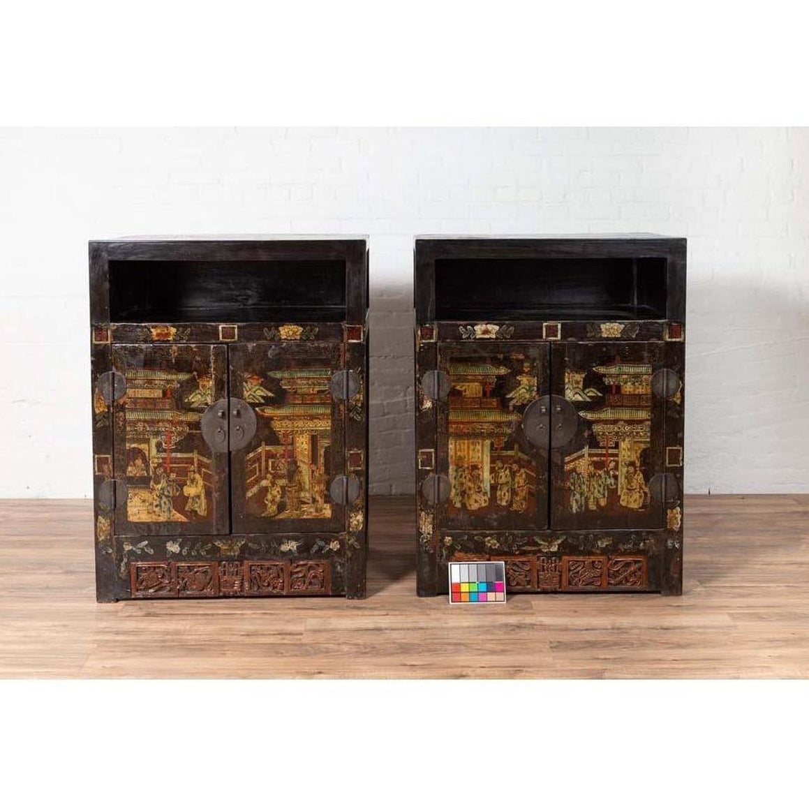 Black lacquered wood Chinese display cabinets with hand painted chinoiserie motifs, round metal handles, on wooden floor.