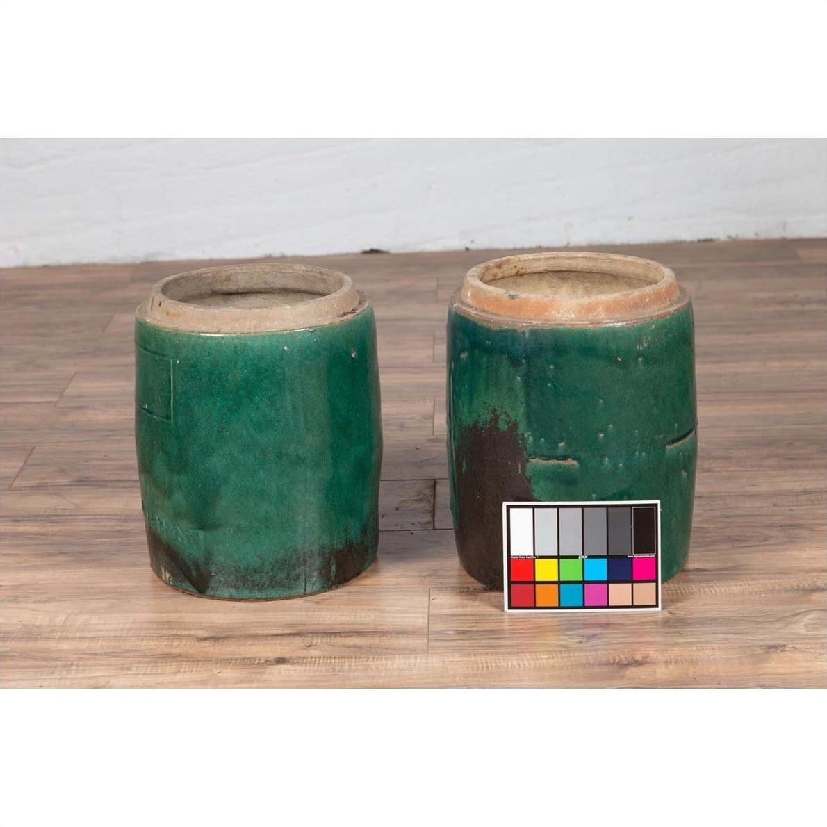 Green glazed ceramic Chinese planters with brown patches on wooden floor beside a color chart, close-up.