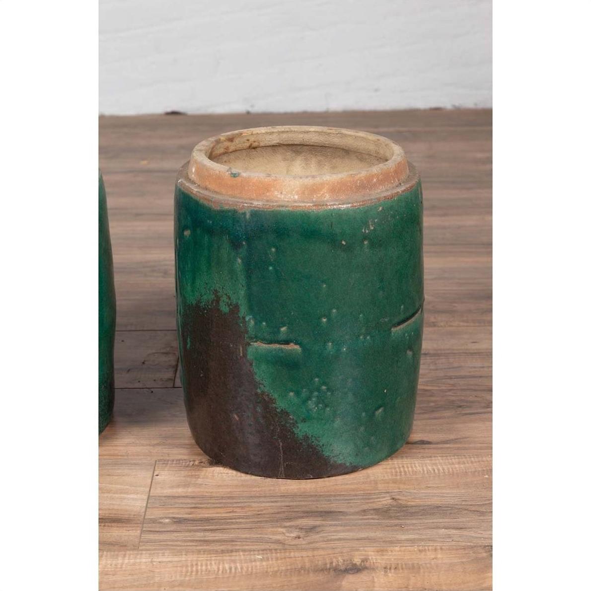 Green glazed ceramic Chinese planters with rustic finish on wooden floor against a white wall.