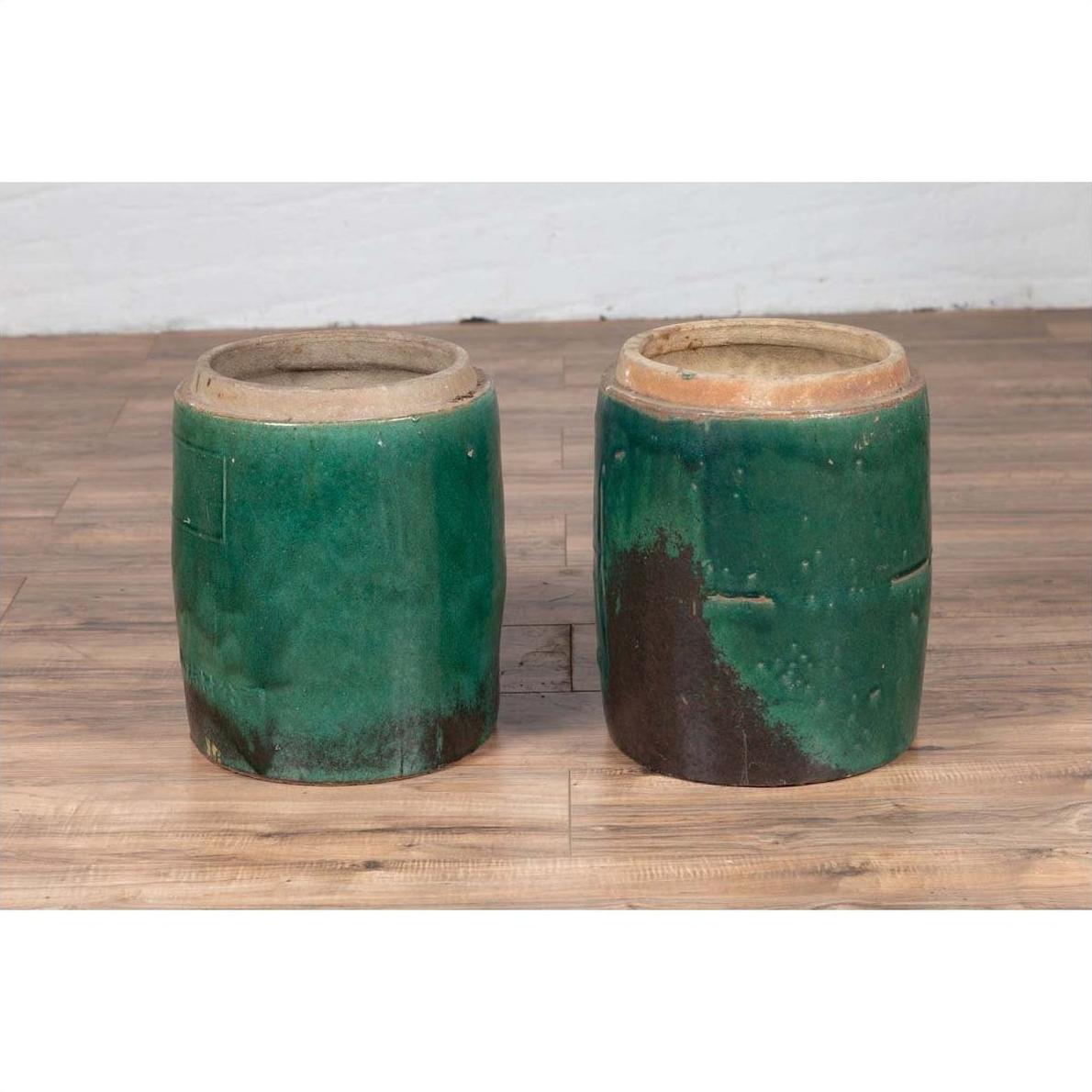 Green glazed ceramic Chinese planters with rustic finish on wooden floor against a white wall.