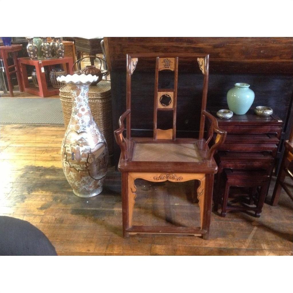 Light wood and rattan arm chairs beside a tall painted vase, blue jar, and nested tables on wooden floor.