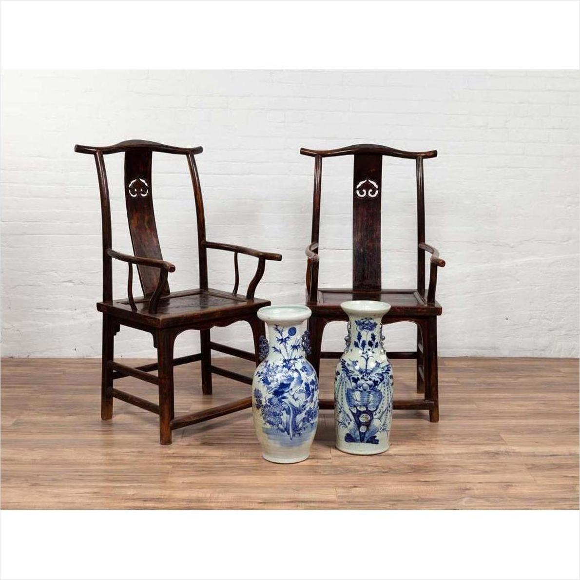 Brown wood Chinese Official's Hat Chairs from 1880s with carved splats, on wooden floor, white brick wall background.