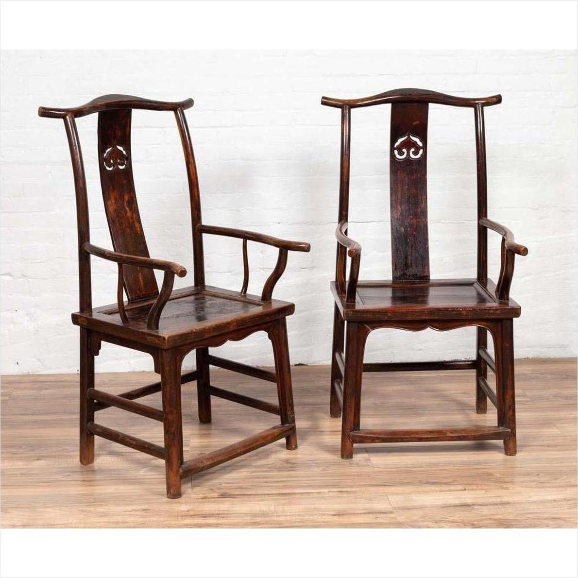 Pair of wood Chinese 1880s Official's Hat Chairs with carved splats on wooden floor by white brick wall.