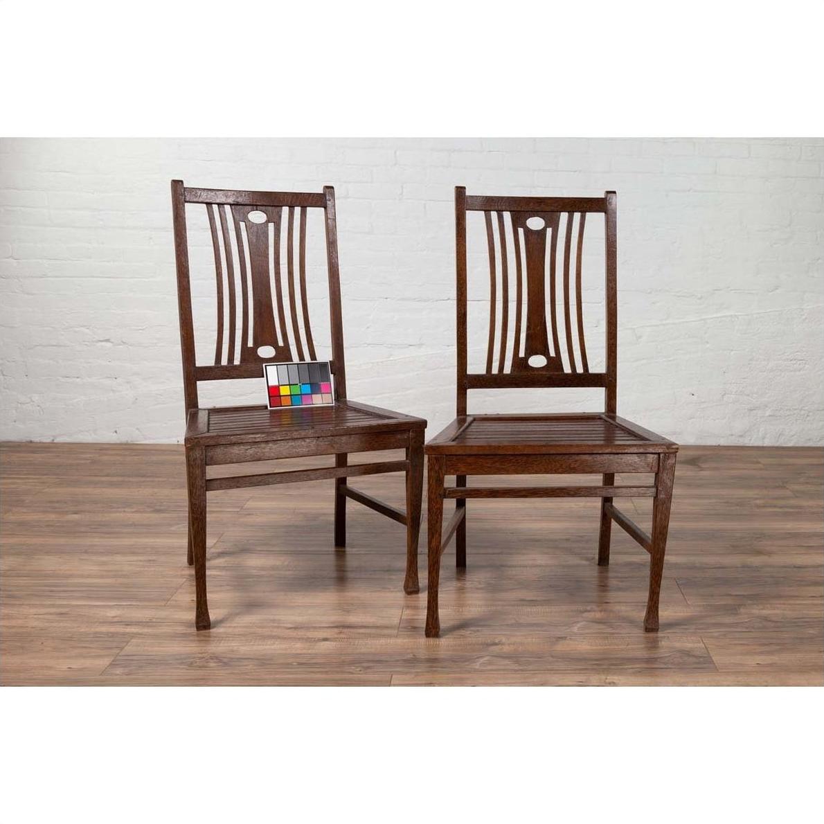 Brown wooden Indonesian side chairs with pierced splats on wood floor, one with color card attached.