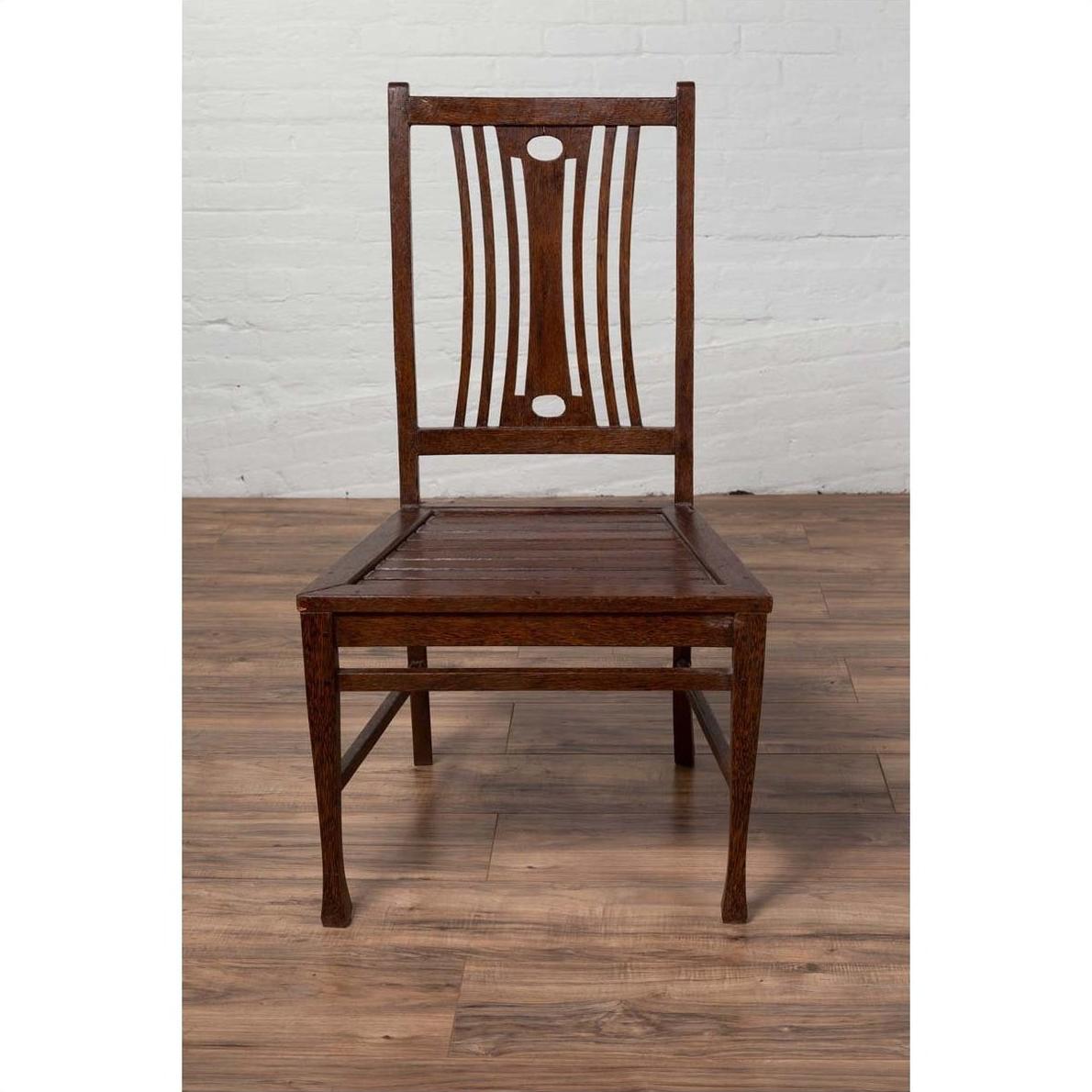 Brown wood Indonesian side chairs with pierced splats on a wooden floor against a white brick wall indoors.