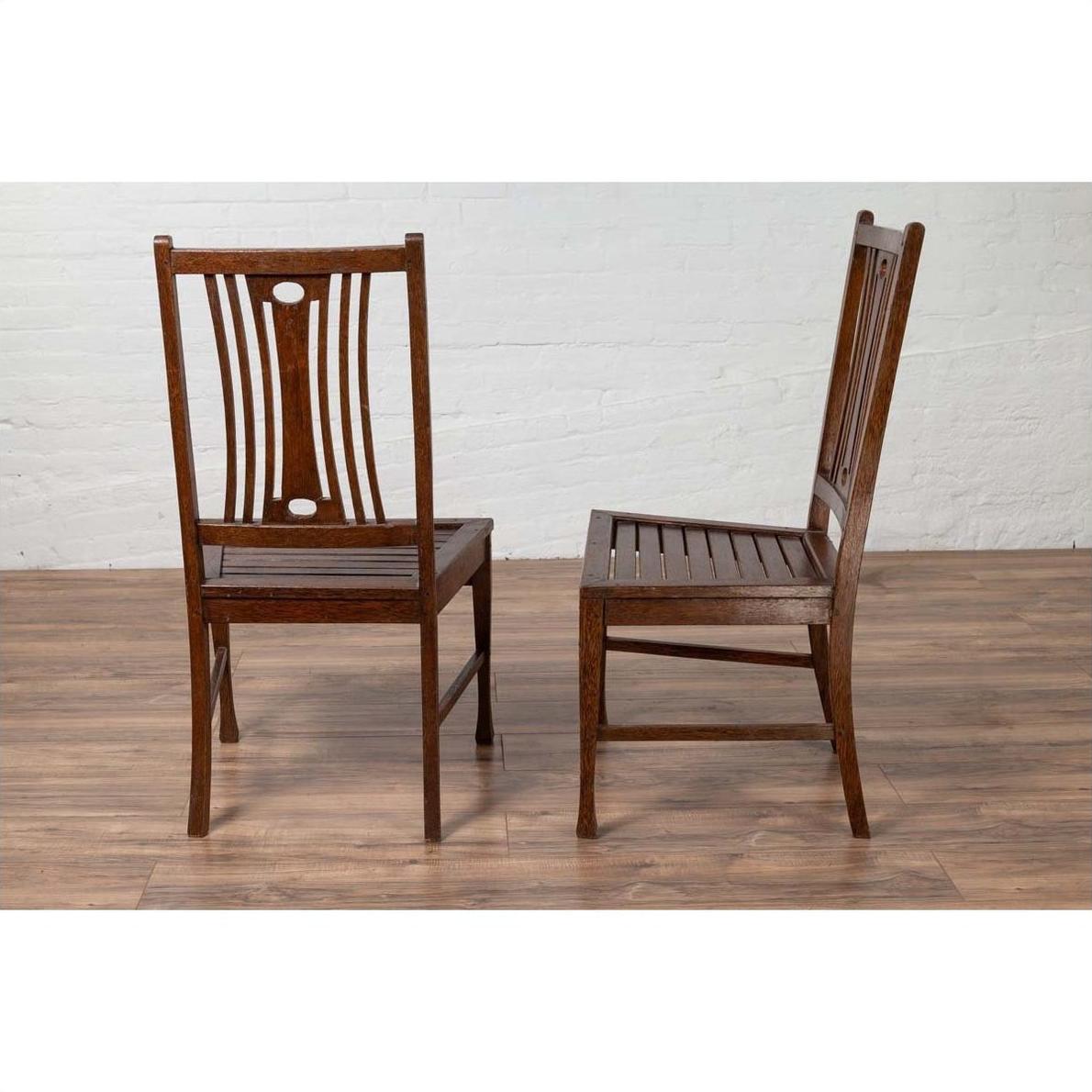 Brown wooden Indonesian side chairs with pierced splats, mid-century style, shown on a wooden floor indoors.