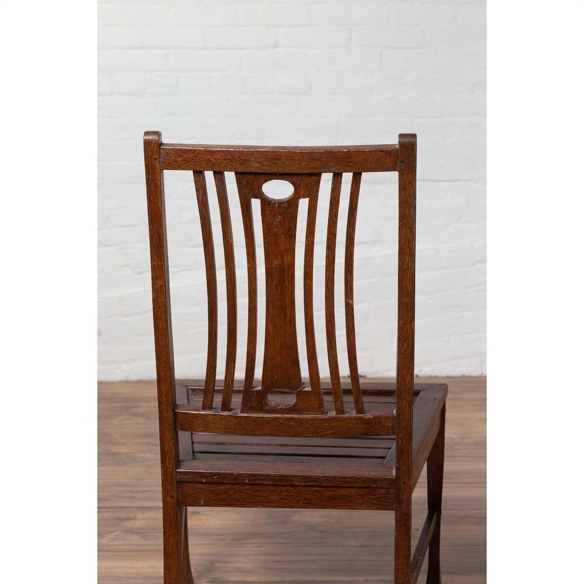 Brown wood Indonesian side chairs with pierced splats on wooden floor against white brick wall, indoors.
