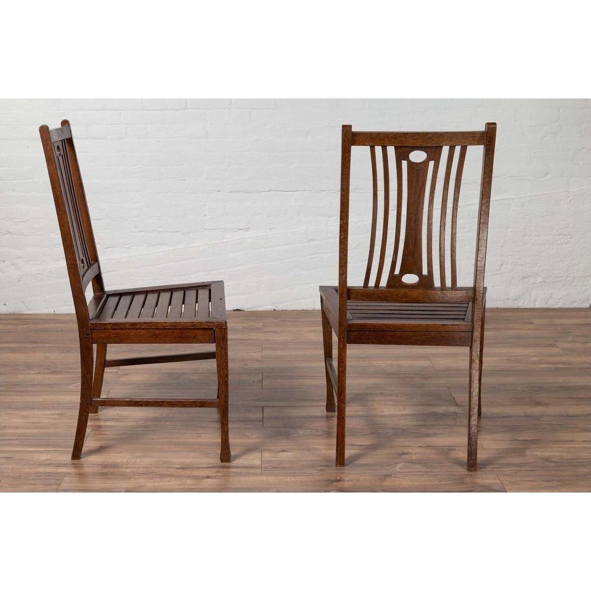 Brown wood Indonesian side chairs with pierced splats on wood floor, white brick wall background, indoor setting.