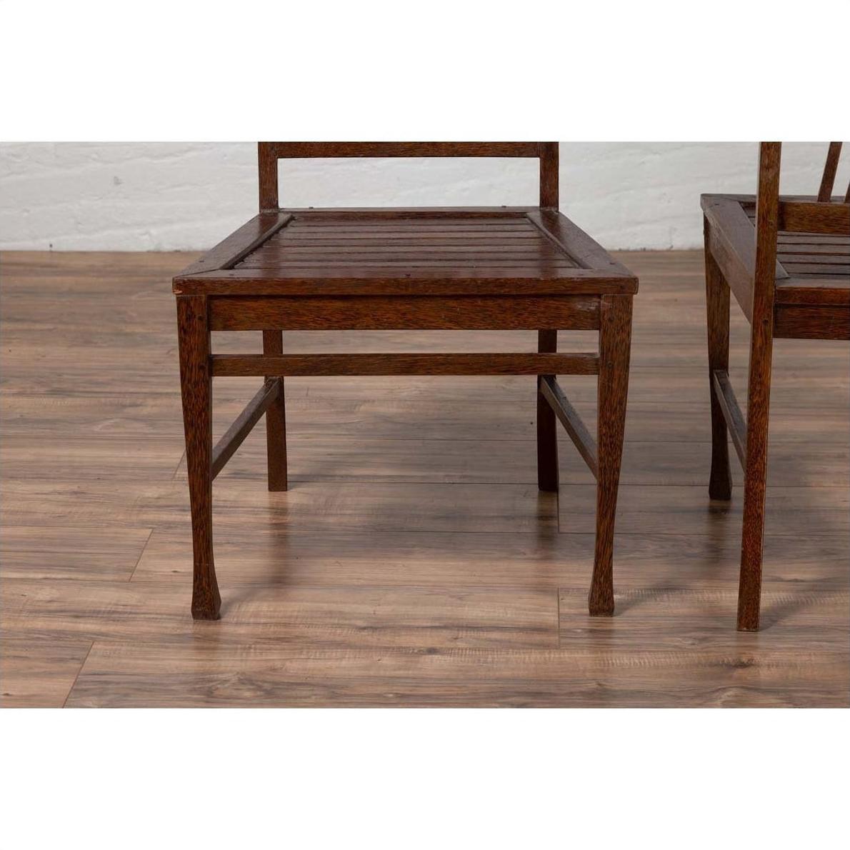 Brown wood Indonesian side chairs with pierced splats on wood floor, right chair partially cropped.