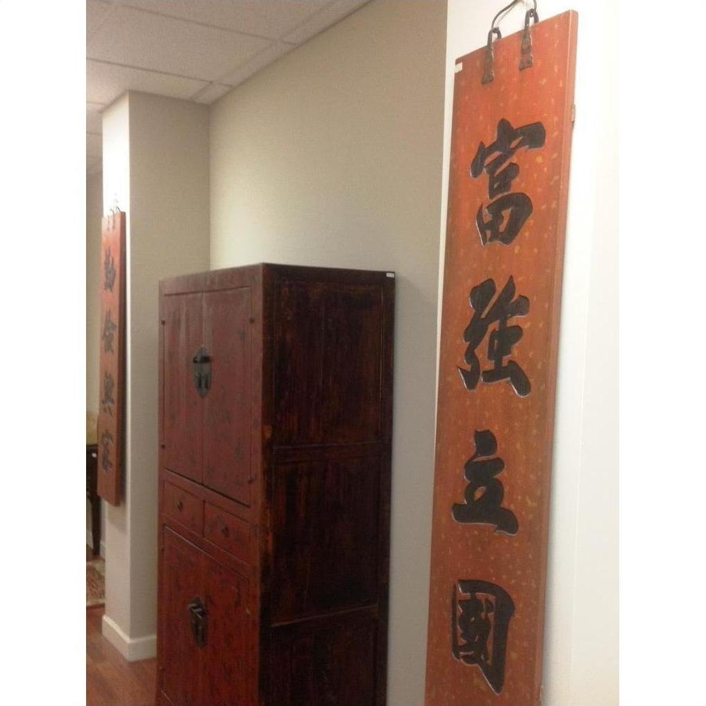 Brown wooden Chinese signs wall art on vertical panels, displayed in a bright hallway with white walls and wood cabinet.