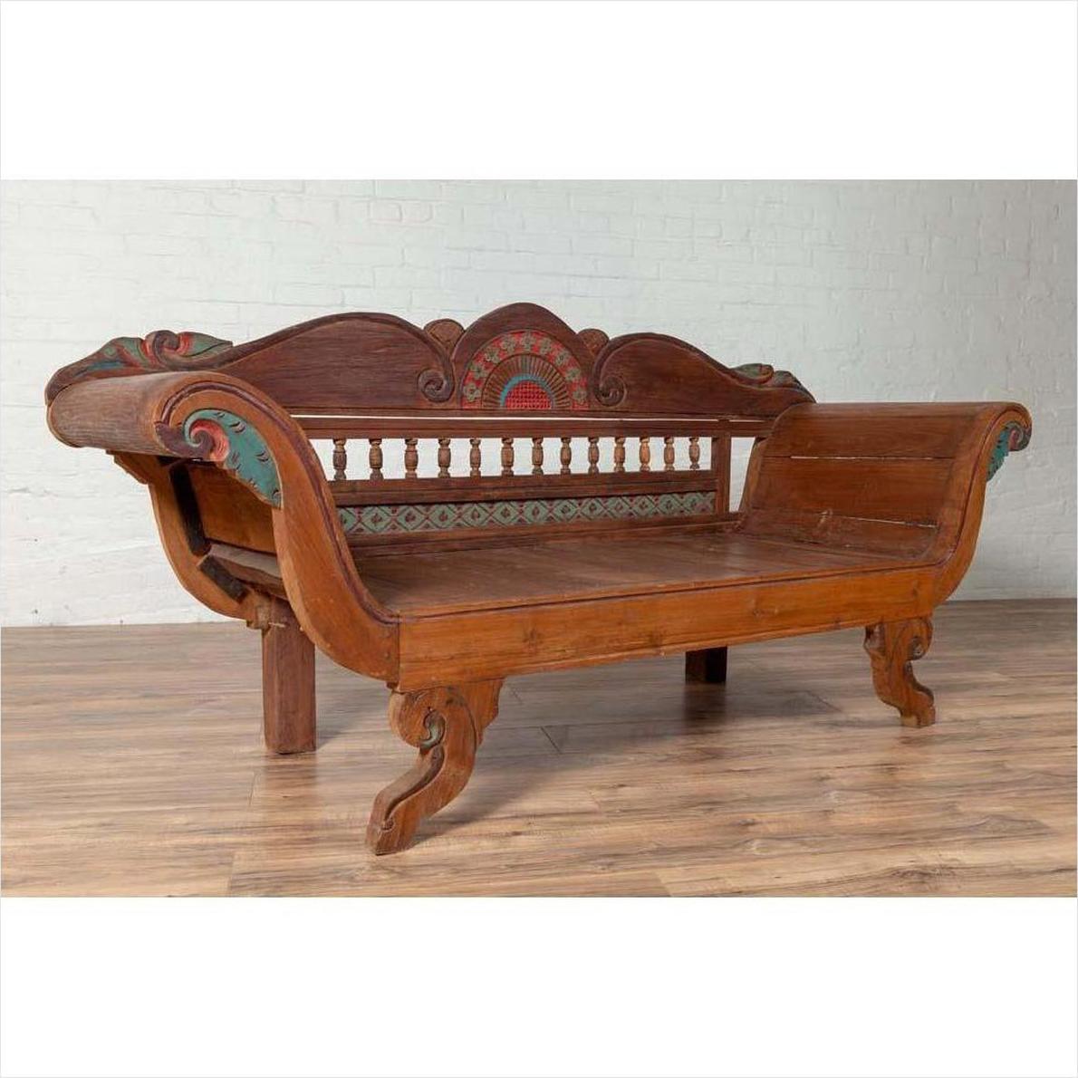 Brown teak wood settee with polychrome décor and out-scrolling arms on wooden floor indoors.
