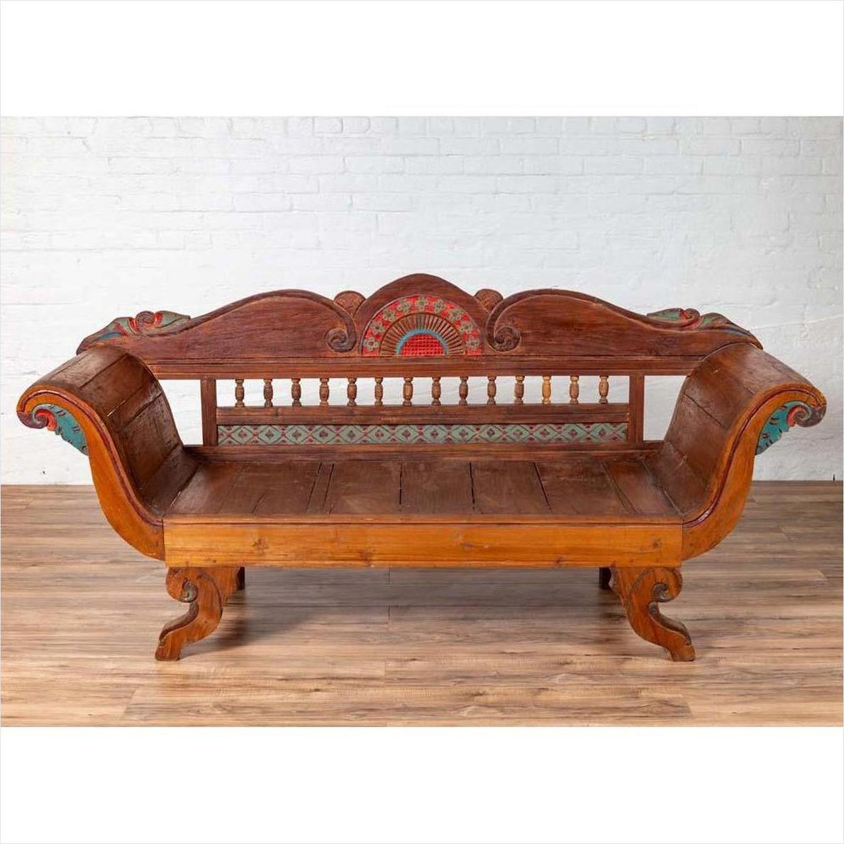 Brown teak wood settee with polychrome décor and out-scrolling arms on a wooden floor indoors.