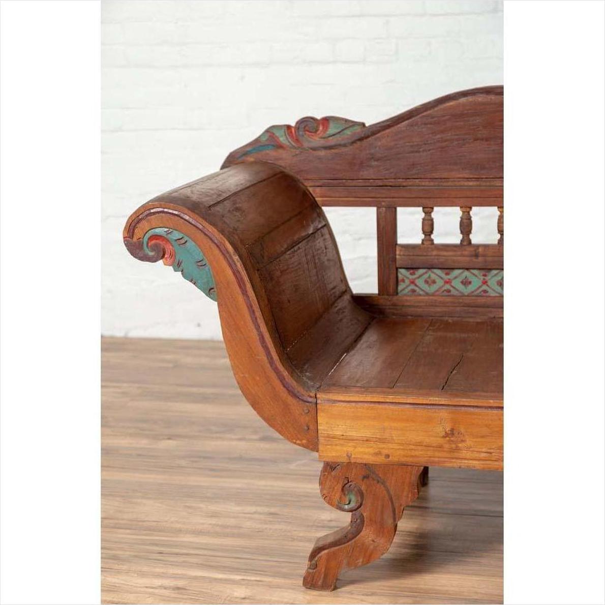 Brown teak wood settee with polychrome décor and out-scrolling arms on a wooden floor indoors.