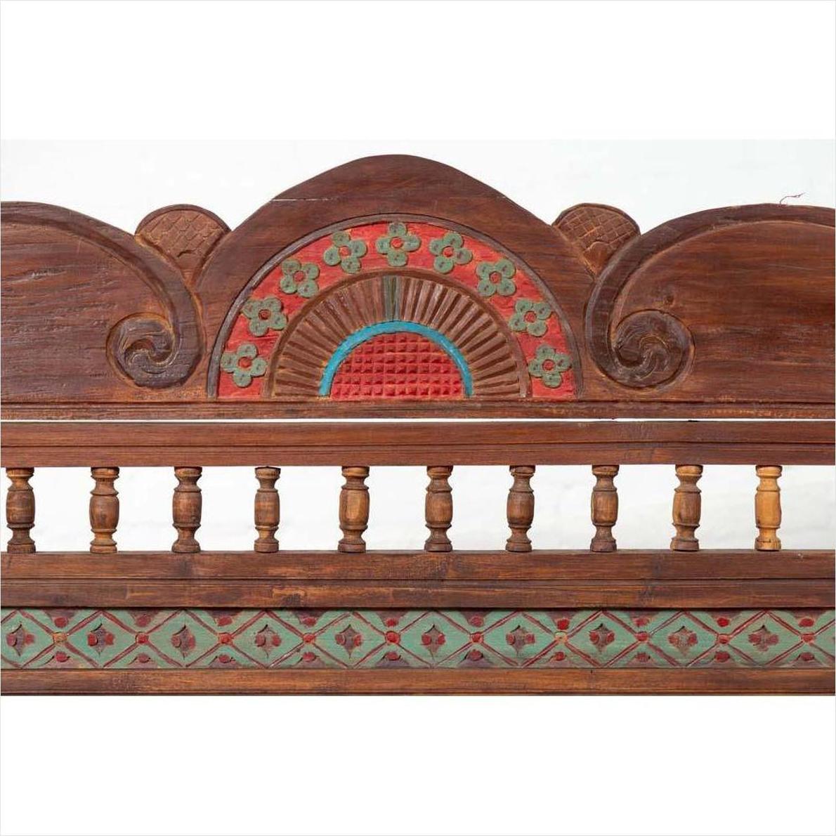 Brown teak wood settee with colorful polychrome decoration and out-scrolling arms, indoor setting.