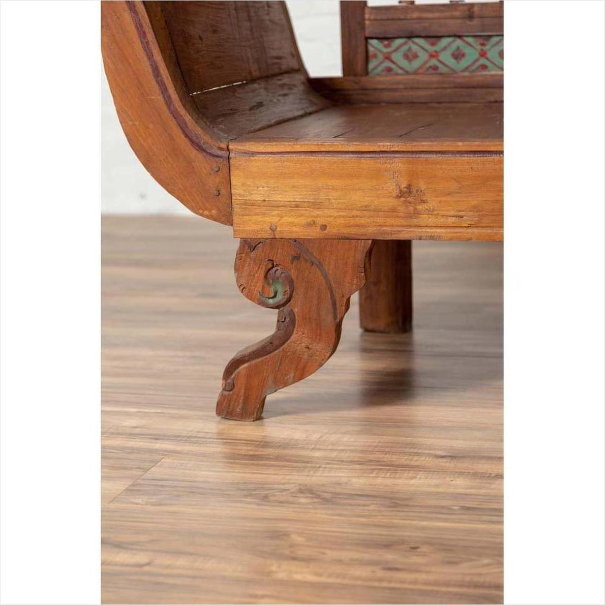 Close-up of brown teak wood settee leg with polychrome décor on polished wooden surface.