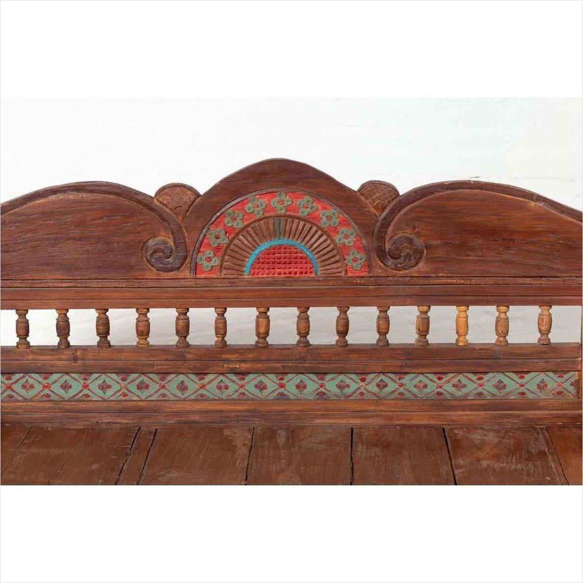 Brown teak wood settee with polychrome décor and out-scrolling arms placed indoors.