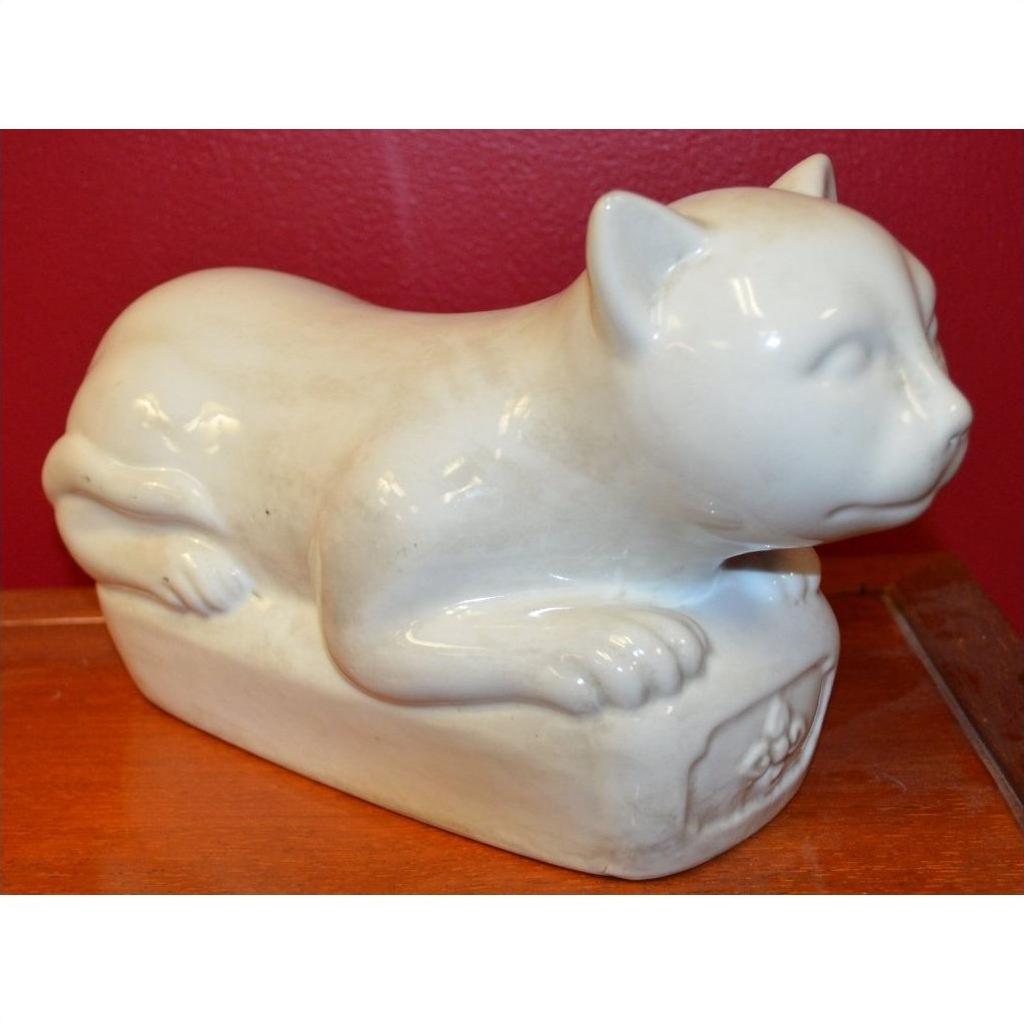 White porcelain reclining cat figure on a wooden base with a vibrant red wall background, close-up view.