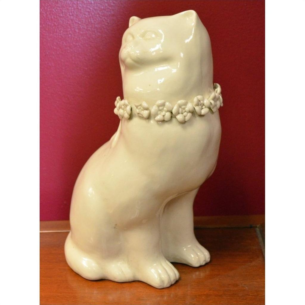 White porcelain cat figurine with head turned to the side on a wooden surface, red wall in background.